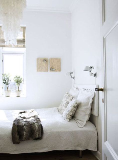 a small neutral bedroom with a small bed, some artworks, potted greenery and a mother of pearl chandelier