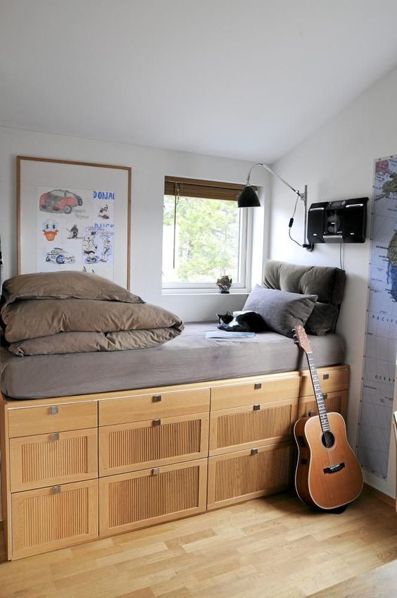 a storage unit with lots of compartments by the window doubles as a comfy daybed, which is an ultimate idea for a small room