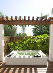 an outdoor bathtub of stone with walls for privacy and lush greenery to make it feel outdoorsy