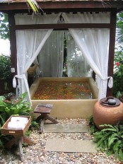 an outdoor stone bathtub with a cover over it and some curtains for privacy, potted greenery refresh the space