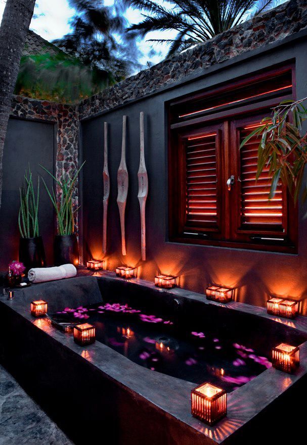 an outdoor stone bathtub with candle lanterns on the edges and tall walls to keep privacy