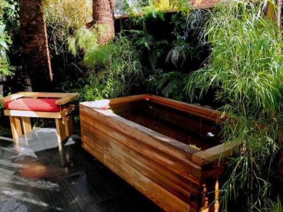 a wooden bathtub placed by a greenery wall plus a simple stool will make up a cool and welcoming outdoor spa
