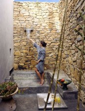 an outdoor waterfall shower with tall stone walls and some greenery and bowls with fruits for a fresh feel