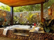 an outdoor bathtub on a stone platform and with stone walls for privacy and potted plants for a fresh and lively feel