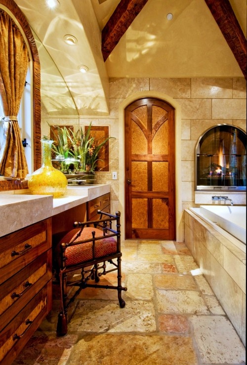 a vintage bathroom clad with stone, with a wooden vanity, a metal chair with red upholstery, a tub clad with tiles and a built-in fireplace in the wall over it