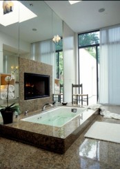 a modern bathroom with a mirror wall, a sunken bathtub clad with tiles, a built-in fireplace and a glazed wall with a curtain
