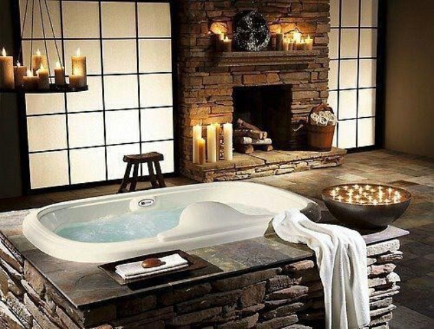 a vintage bathroom clad with faux stone, with a tub clad with it, too, a fireplace, lots of candles is a real relaxation sanctuary that you'll never want to leave