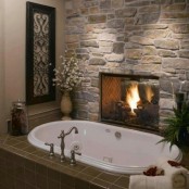 a vintage bathroom with a stone wall with a built-in fireplace, a bathtub clad with green tiles and some greenery