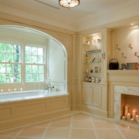 a creamy vintage bathroom with a tub placed by the window, with built-in shelves, a fireplace and lots of candles for a chic and stylish look