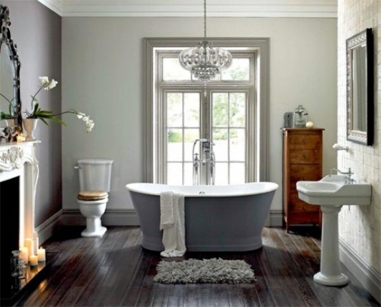 a vintage bathroom with a dark floor, a vintage fireplace with candles, a grey bathtub, a free-standing sink and a crystal chandelier