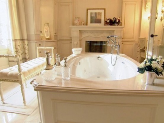 a creamy vintage bathroom with a fireplace, a bathtub clad with paneling, a vintage bench and some blooms and candles