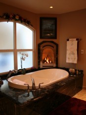 a vintage earth toned bathroom with a sunken bathtub, a built-in fireplace, an arched window with frosted glass