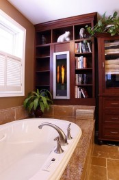 a dark-stained storage unit with open shelves and cabinets, a bathtub clad with tan tiles and some greenery to refresh the space