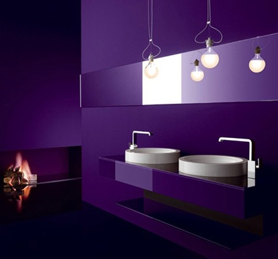 a sleek purple bathroom with a double vanity, pendant bulbs, a long mirror and an open fireplace looks very unusual and edgy