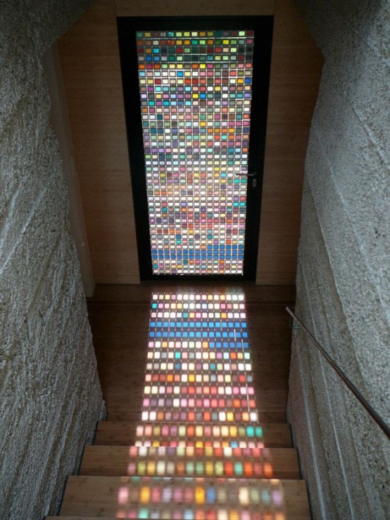 a modern entryway with light-stained wooden walls, a door completely with colorful stained glass that fills the space with color and makes it interesting
