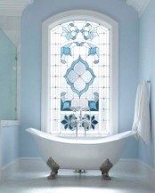 an airy and light-filled serenity blue bathroom with a shower space, with a large stained glass window and a vintage clawfoot bathtub