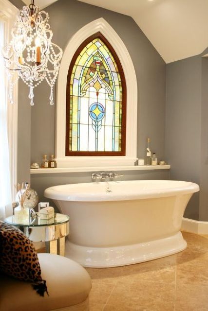 a vintage farmhouse bathroom with grey walls, with a refined stained glass window, with an oval tub and a crystal chandelier