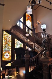 a refined vintage space with a dark-stained carved staircase, with a piano and beautiful lamps, with stained glass windows that keep privacy and add color