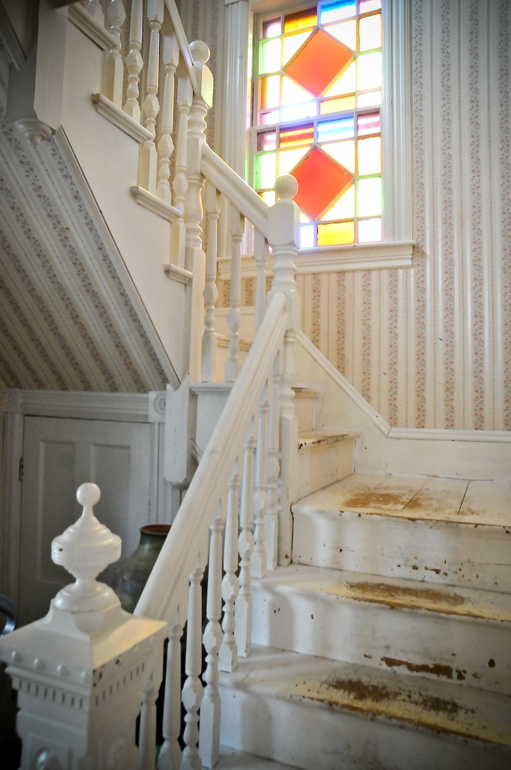 a neutral shabby chic space with catchy wallpaper and a vintage staircase, with stained glass windows is a lovely space