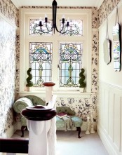 an adorable vintage nook at the staircase, with beautiful botanical wallpaper and a green vintage daybed, with a vintage chandelier and mirrors