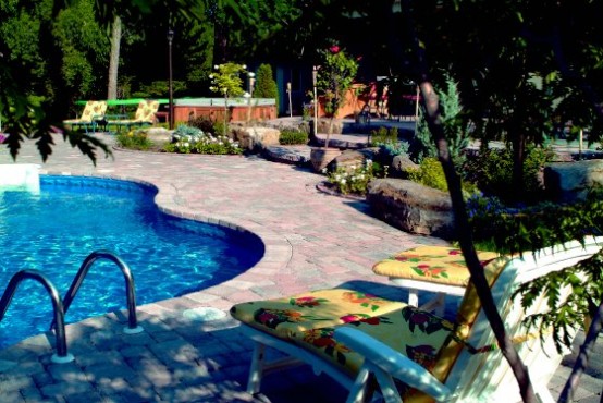 a catchily shaped pool with a stone deck, greenery and blooms and loungers with bright upholstery, cushions and pillows