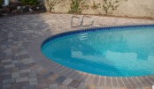 a blue oval pool with a beige stone deck and a bit of greenery around are a perfect combo that you may rock for your backyard – nothing else is needed