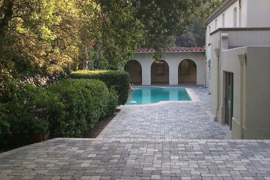 an elegant and refined outdoor space with a catchily shaped pool, a stone deck and greenery and trees around is amazing