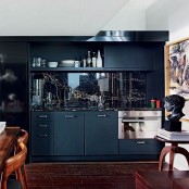 a matte black kitchen with a glossy black marble backsplash and some stained dining furnniture is a cool space ot be in
