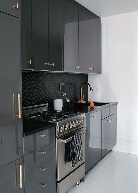 a glossy black kitchen with black chevron tiles on the backsplash and gold fixtures is a cool and chic idea in a classic color
