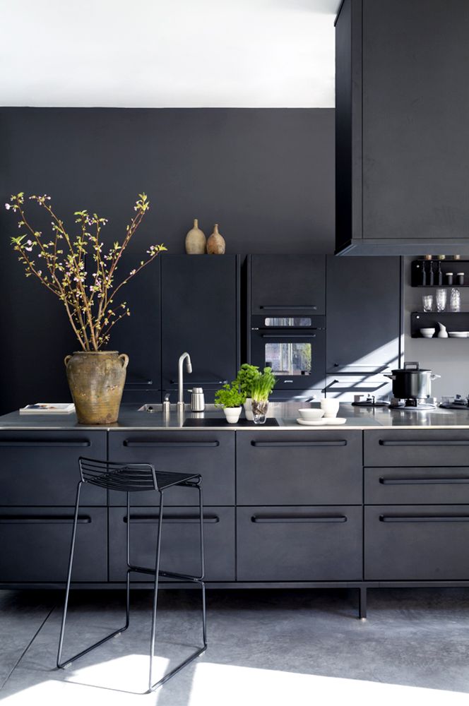 a refined minimalist matte black kitchen of metal, with a large kitchen island, a hood, white countertops and black stools