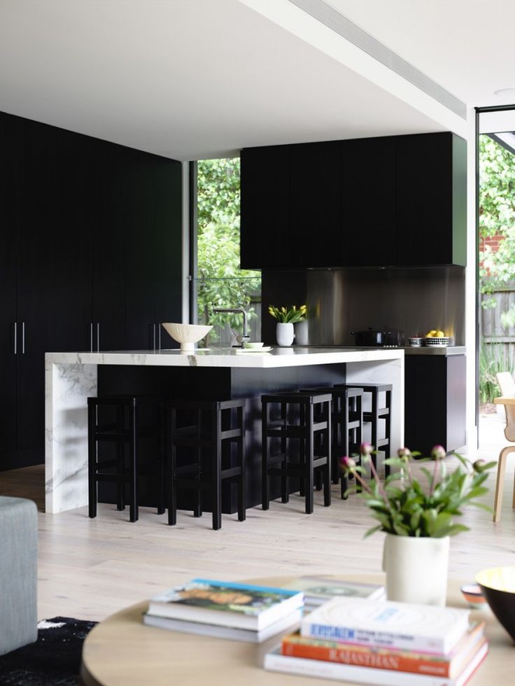 a black kitchen with a black and white kitchen island, black stools and a white ceiling that makes the space feel fresh and airy