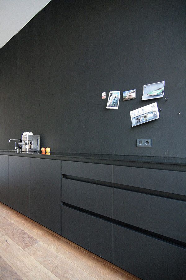 a minimalist matte black kitchen with only lower cabinets, a glossy countertop and a sink, some photos on the wall is a chic and cool space