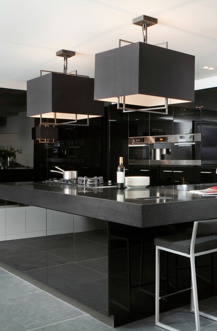 a minimalist black kitchen with glossy surfaces, built in appliances, black pendant lamps and black stools