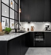 a matte black kitchen with sleek panels, a white backsplash and white stone countertops, an internal window with black framing