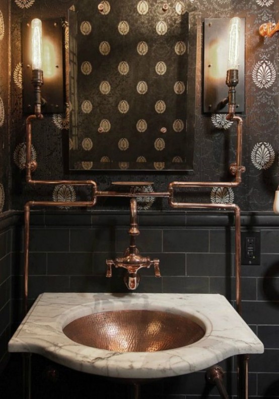 a dark vintage industrial bathroom with black wallpaper walls, black tiles, a stone adn copper sink and copper pipes exposed is a chic space