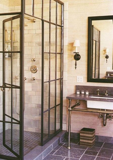 a vintage industrial bathroom with white and grey tiles, a shower space, a sink on a pipe and stone stand and a mirror in a black frame is a chic space