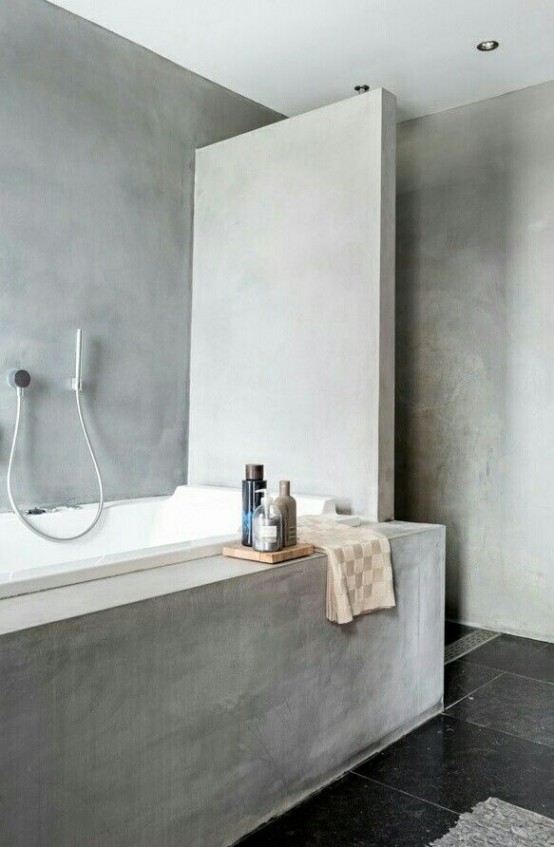 a minimalist industrial bathroom fully done with concrete, with a half wall and with black tiles on the floor is practical