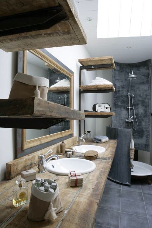 a vintage industrial bathroom with white walls, concrete tiles, rough wooden shelves and a vanity plus a large mirror