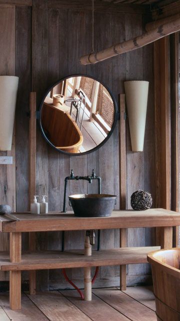 a rustic industrial bathroom with wooden walls and furniture, a round mirror, a cone, a metal sink and a vine ball
