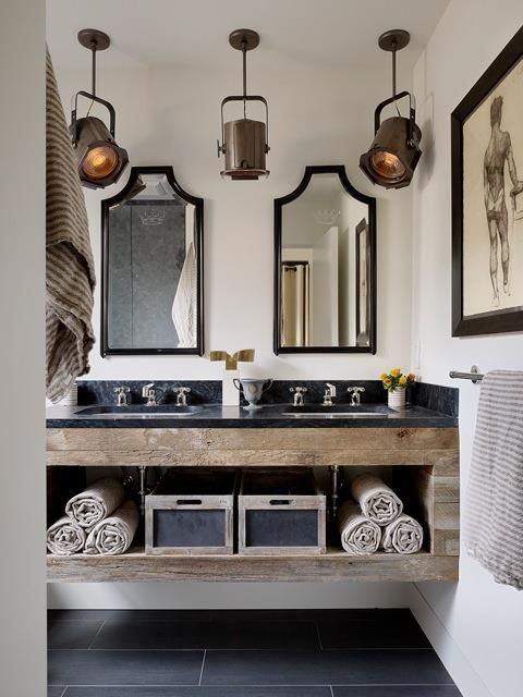 a rustic industrial bathroom with a floating rough wood vanity with an open storage, pendant lamps, a duo of mirrors and some artworks is very elegant