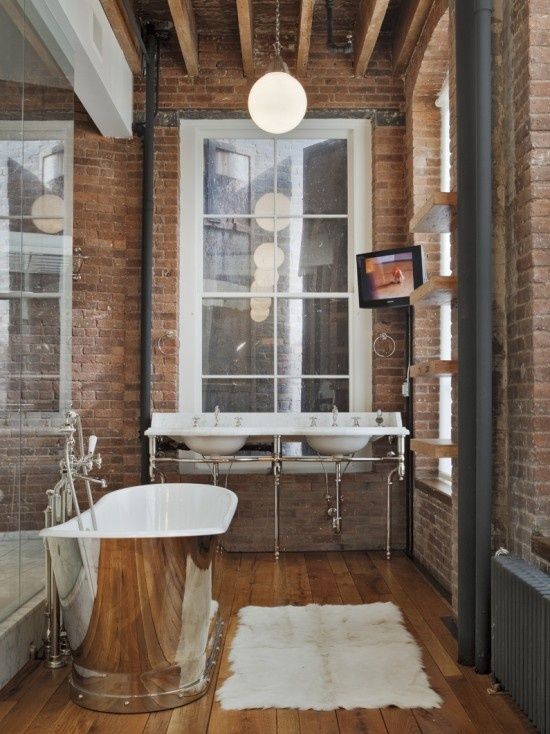 a vintage industrial bathoom with brick walls, a double sink, a metal clad bathtub and pendant lamps is very chic