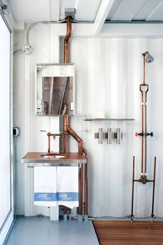 a vintage industrial bathroom with white corrugated steel walls, a wooden floor, exposed pipes, a mirror and lamps