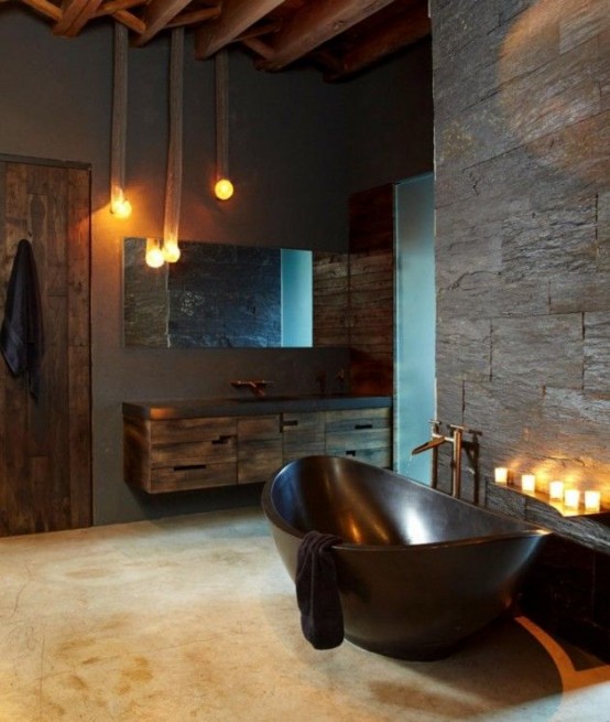 a mascauline meets industrial bathroom with concrete and faux stone walls, rough wooden furniture and a door, a polished stone bathtub and candles and pendant lamps