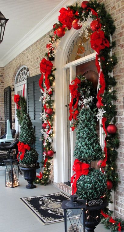 Christmas topiaries with red bows, lanterns with lights, an evergreen garland with red ribbons and lights and red ornaments