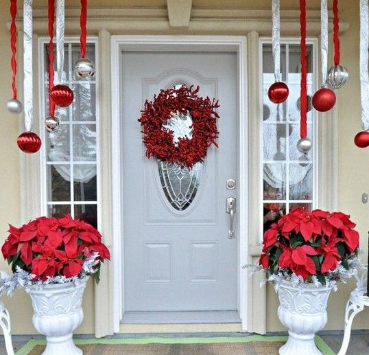 a red, white and silver porch with hanging red and silver ornaments, red blooms in urns, a red berry wreath on the front door