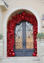 a front door decorated with a super lush red ornament garland that frames both doors and catches an eye