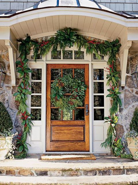 simple and natural Christmas front door styling with an evergreen garland with red blooms and a matching large wreath on the door