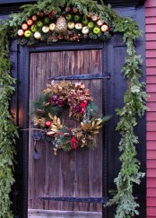 Christmas front door decor with an evergreen garland, pinecones, apples and a quirky wreath with pinecones, apples, dried leaves and berries