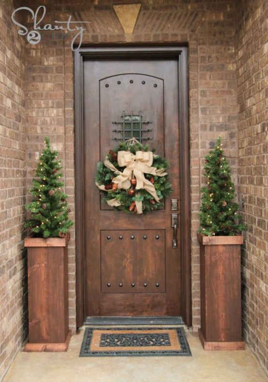 rustic front door Christmas styling with mini tree with pinecones and lights and a wreath with pinecones, ornaments and a bow on top