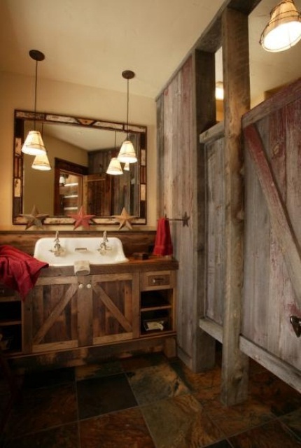 a rough wooden bathroom clad with reclaimed wood and with a matching vanity, with vintage pendant lamps and bold red towels